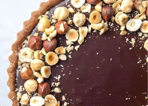 Delicious Chocolate Hazelnut Tart topped with hazelnuts and chocolate glaze.