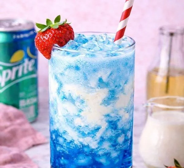 Glass of blue raspberry dirty soda with ice and fresh fruit garnish.