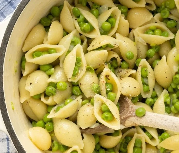 Bowl of fresh pasta with peas garnished with herbs and parmesan cheese