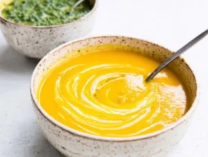 Bowl of vibrant carrot soup garnished with chermoula sauce.