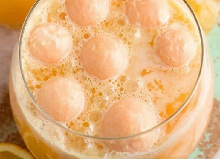 Delicious Orange Sherbet Punch served in a glass bowl with colorful fruit garnishes.