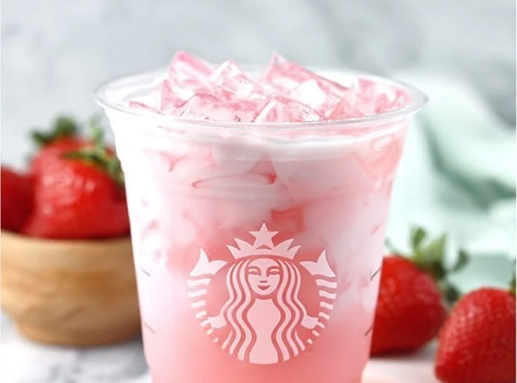 A refreshing Starbucks Copycat Pink Drink in a glass with strawberries and coconut milk.