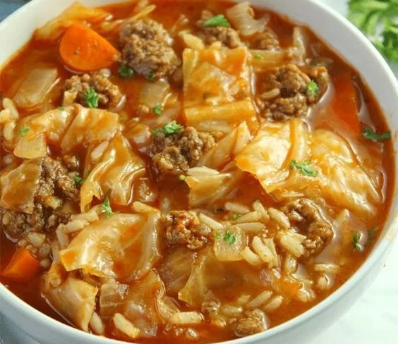 Bowl of cabbage roll soup with beef and chopped vegetables on a wooden table.