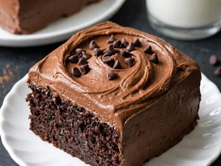 Chocolate zucchini cake topped with cream cheese frosting on a wooden table