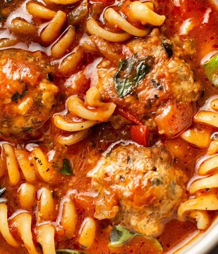 A delicious bowl of Italian meatball soup garnished with fresh herbs and vegetables.