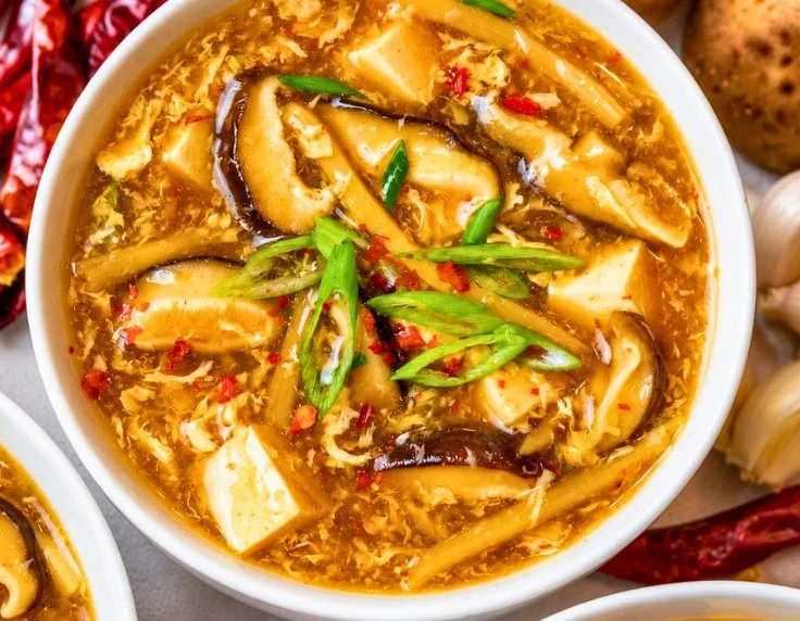 Bowl of hot and sour soup with tofu and mushrooms served in a traditional Chinese dish.