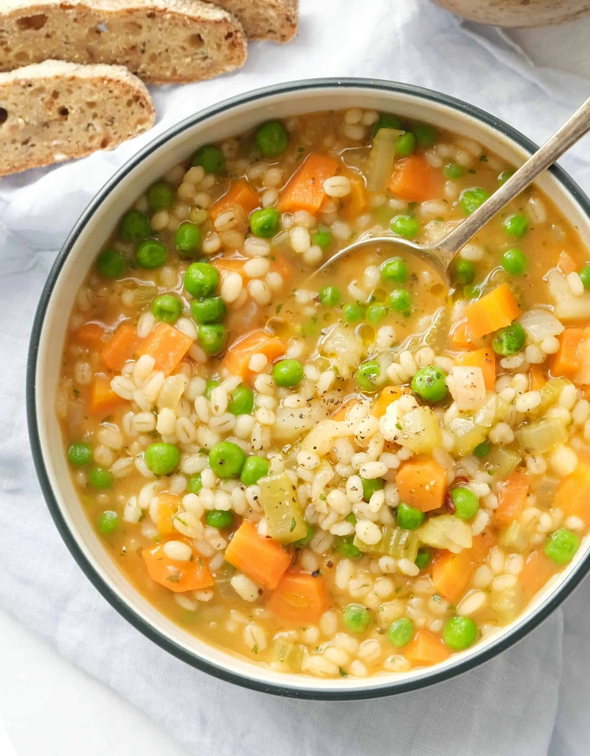 Healthy vegetable barley soup in a bowl with fresh vegetables and herbs